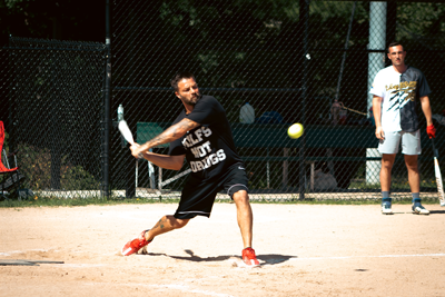 man swinging baseball bat at a softball pitch